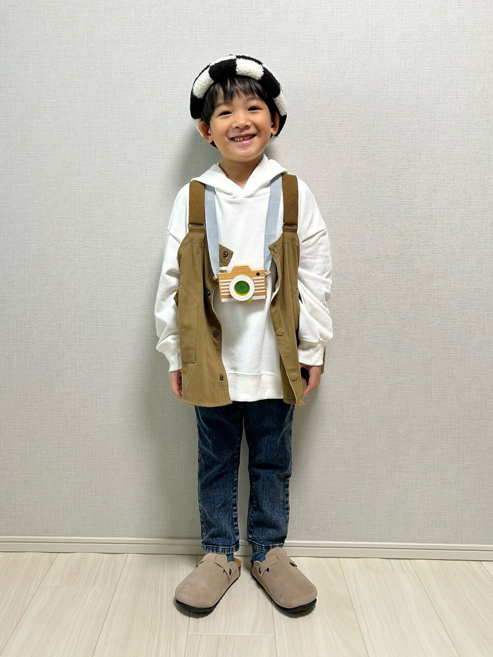 ホワイト系のパーカー、ベージュ系のベスト、ベージュ系のサンダルを着用したキッズの冬コーディネートの2枚目の写真