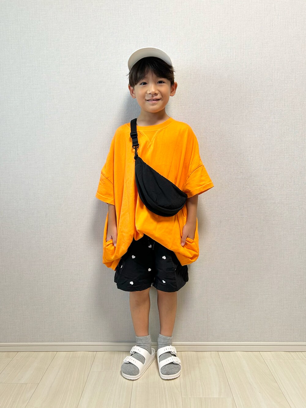 オレンジ系のワンピース、ブラック系のその他パンツ、ホワイト系のサンダルを着用したキッズの夏コーディネートの2枚目の写真