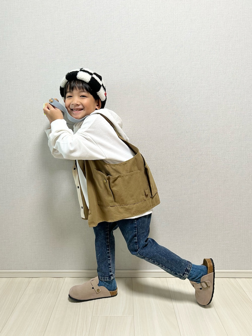 ホワイト系のパーカー、ベージュ系のベスト、ベージュ系のサンダルを着用したキッズの冬コーディネートの3枚目の写真