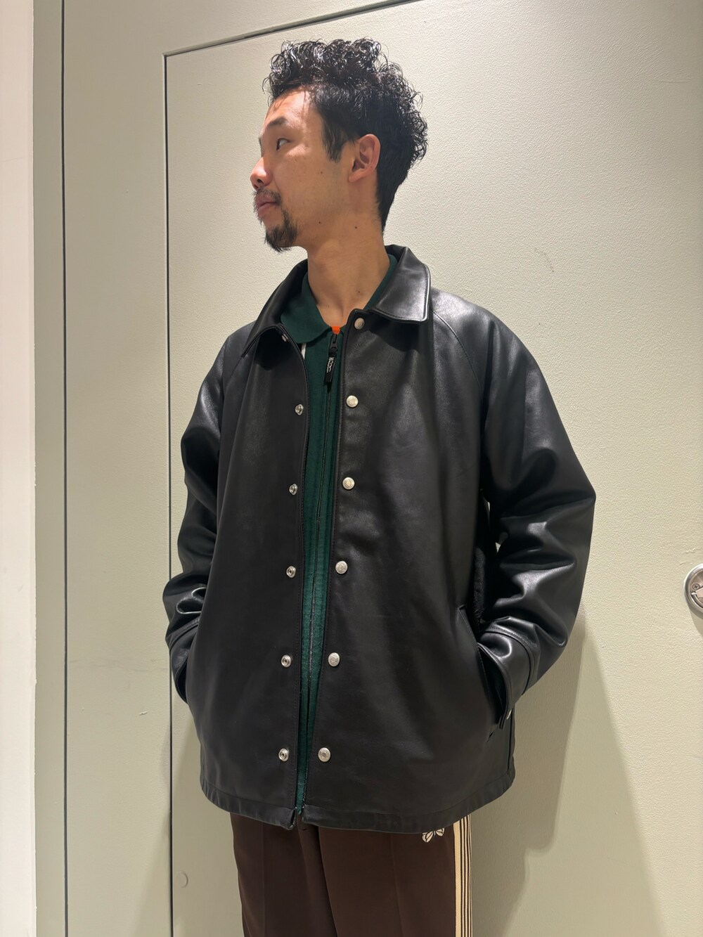 ブラック系のライダースジャケット、グリーン系のニット/セーター、ブラック系のモカシン/デッキシューズを着用したメンズの冬コーディネートの2枚目の写真