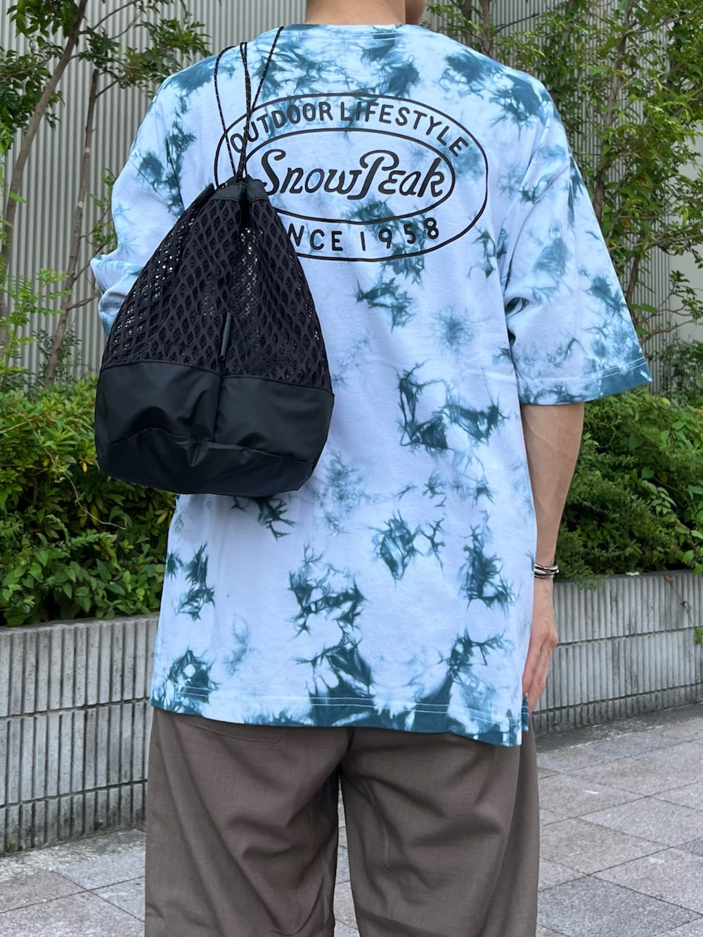 ブルー系のTシャツ/カットソー、ブラック系のバックパック/リュック、ブラウン系のスラックスを着用したメンズの夏コーディネートの2枚目の写真