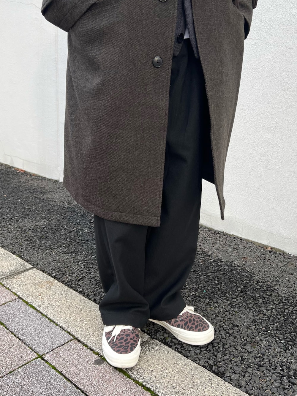 グリーン系のステンカラーコート、ブラック系のカーディガン/ボレロ、ブラック系のスラックスを着用したメンズの秋コーディネートの4枚目の写真
