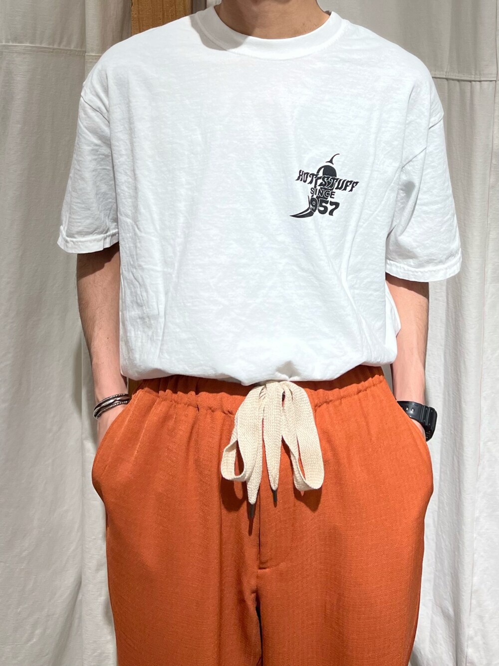 ホワイト系のTシャツ/カットソー、オレンジ系のスラックス、ブラック系のサンダルを着用したメンズの春コーディネートの3枚目の写真