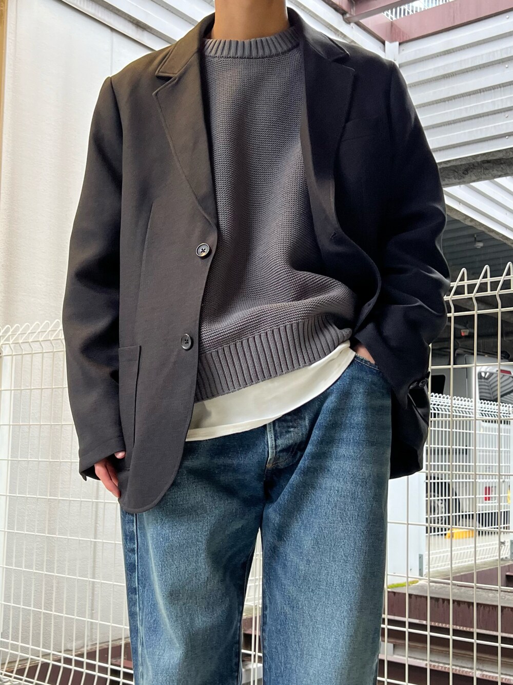 ブラック系のテーラードジャケット、グレー系のニット/セーター、ブルー系のデニムパンツを着用したメンズの春コーディネートの2枚目の写真