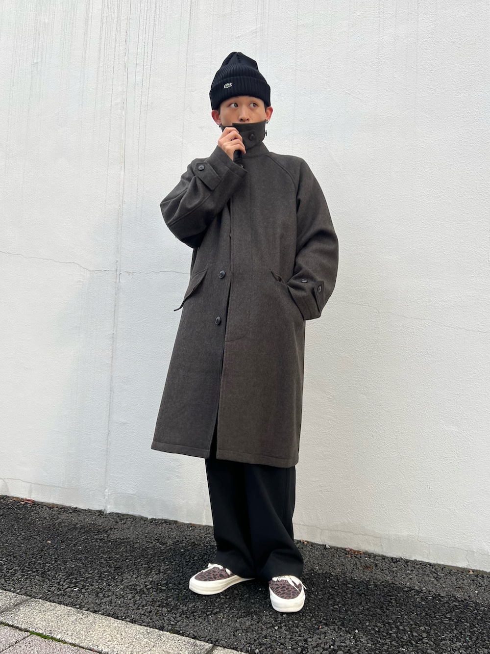 グリーン系のステンカラーコート、ブラック系のカーディガン/ボレロ、ブラック系のスラックスを着用したメンズの秋コーディネートの2枚目の写真