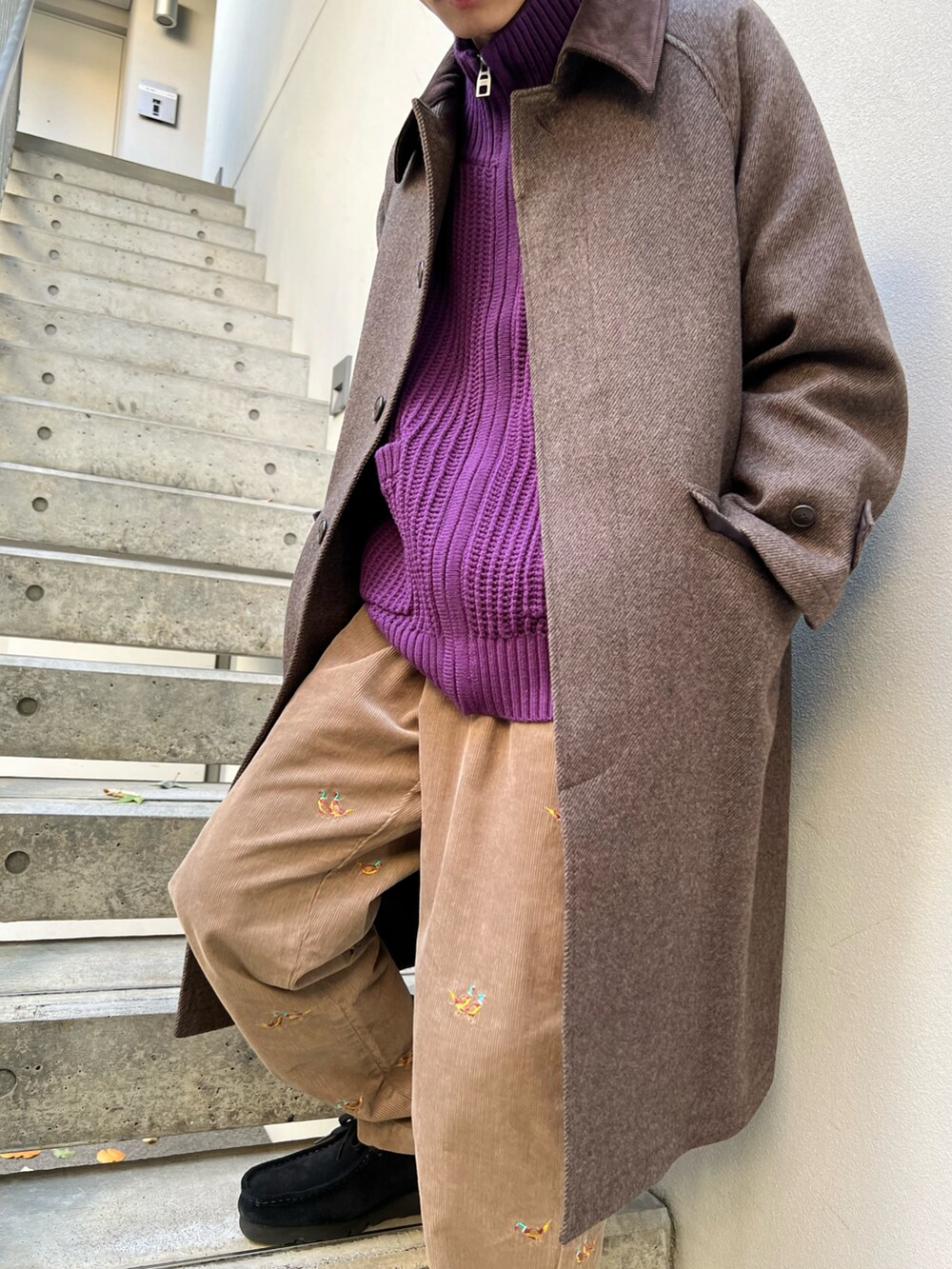 ブラウン系のステンカラーコート、パープル系のニット/セーター、ブラック系のモカシン/デッキシューズを着用したメンズの冬コーディネートの2枚目の写真
