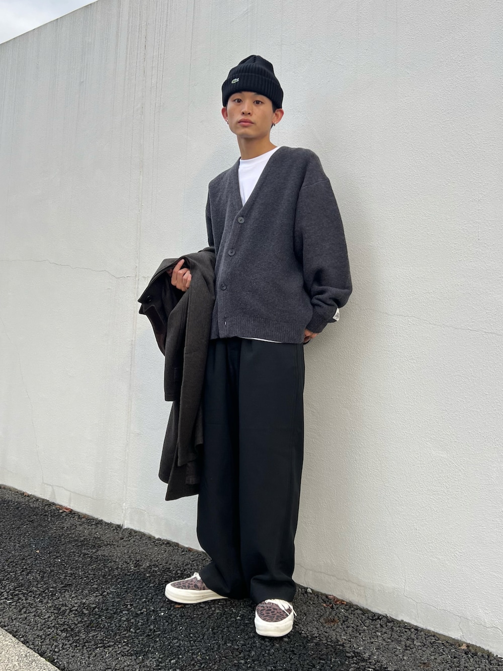 グリーン系のステンカラーコート、ブラック系のカーディガン/ボレロ、ブラック系のスラックスを着用したメンズの秋コーディネートの3枚目の写真