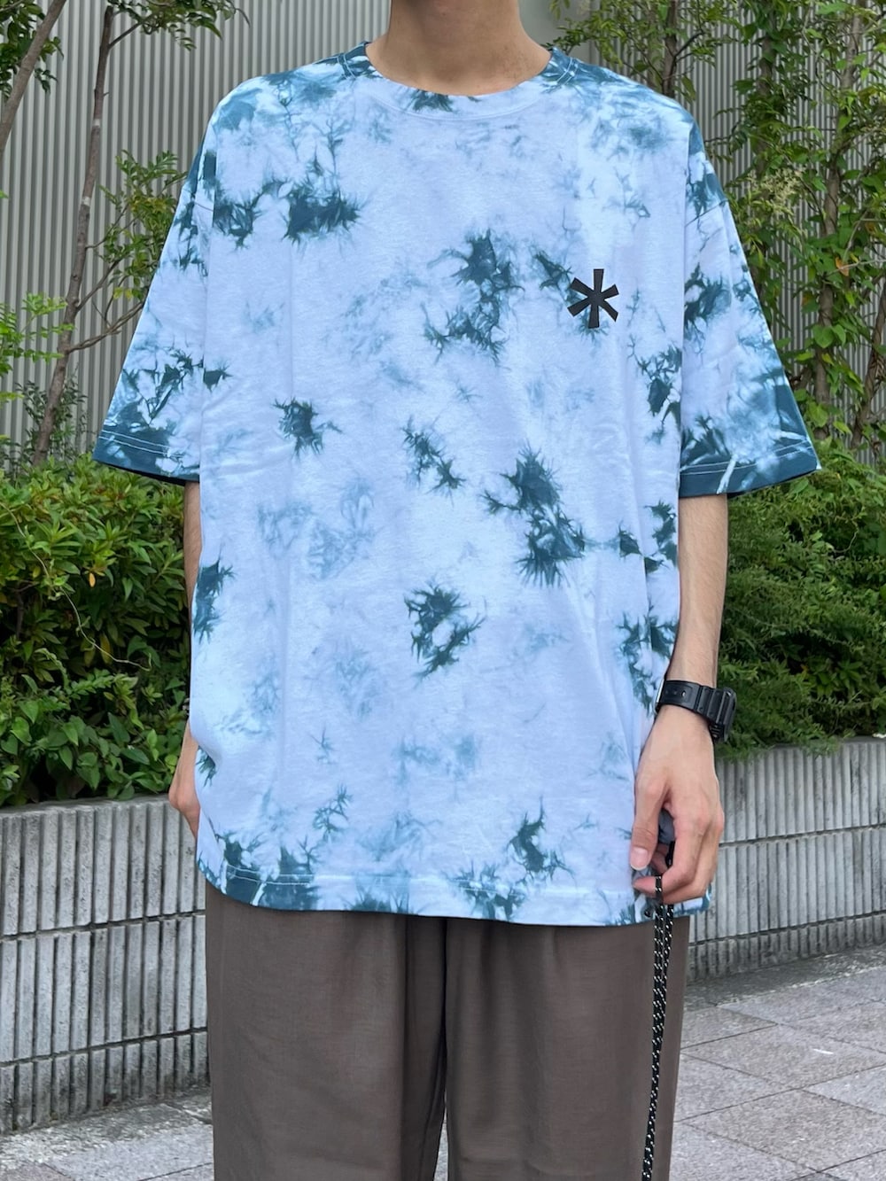 ブルー系のTシャツ/カットソー、ブラック系のバックパック/リュック、ブラウン系のスラックスを着用したメンズの夏コーディネートの3枚目の写真