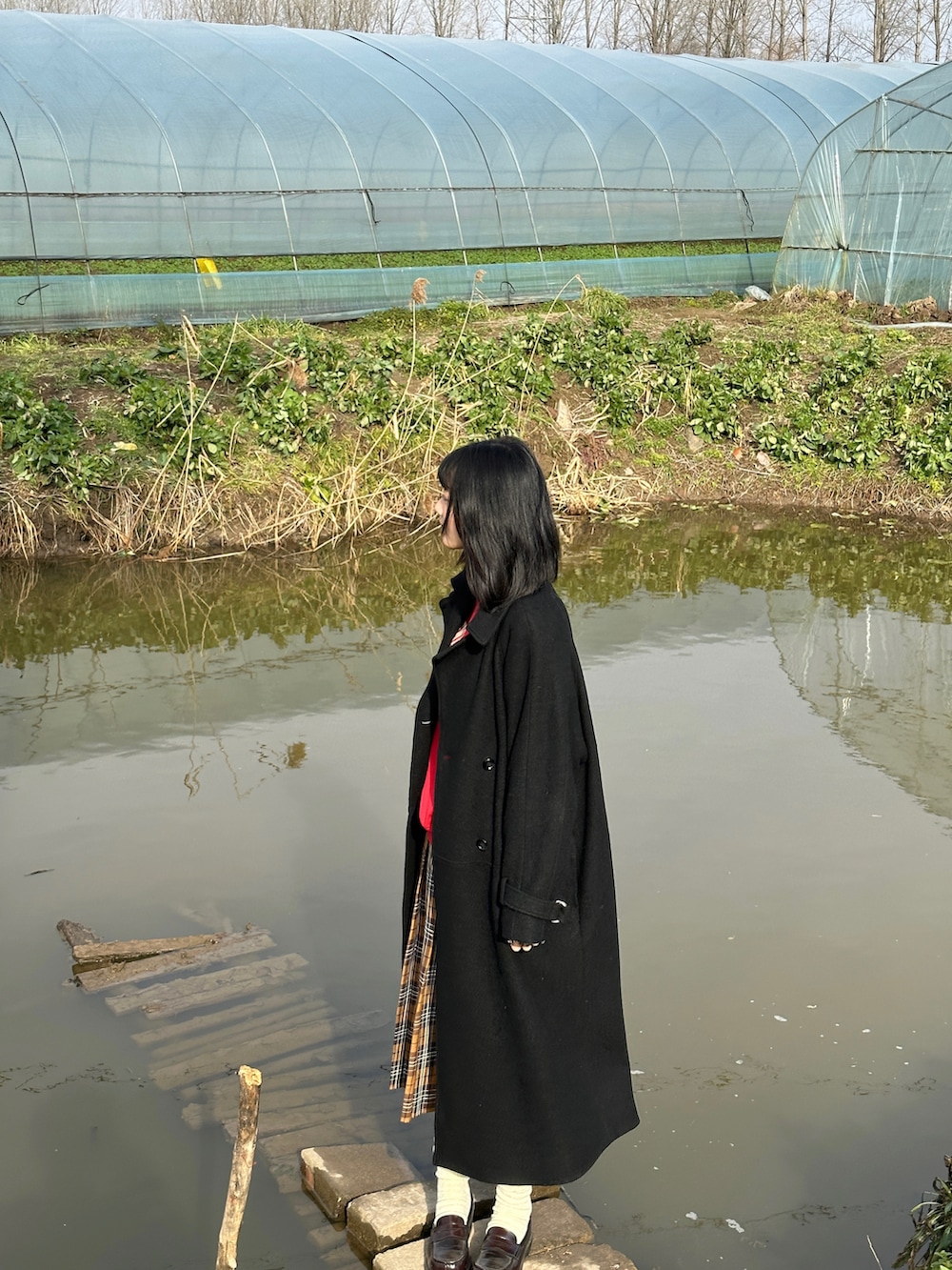 レッド系のスウェット、ブラック系のチェスターコート、ブラウン系のスカートを着用したレディースの冬コーディネートの2枚目の写真