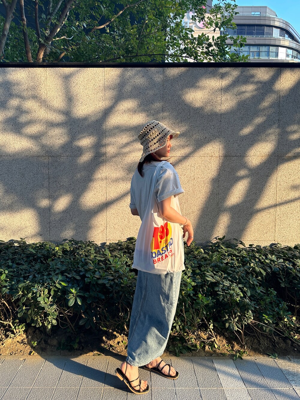 ベージュ系のTシャツ/カットソー、ホワイト系のエコバッグ/サブバッグ、ブラック系のサンダルを着用したレディースの夏コーディネートの2枚目の写真