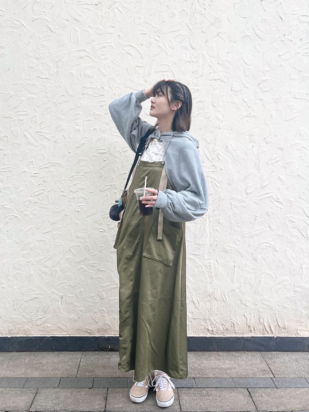 グリーン系のジャンパースカート、ベージュ系のスニーカー、ブラック系のショルダーバッグを着用したレディースの春コーディネートの2枚目の写真