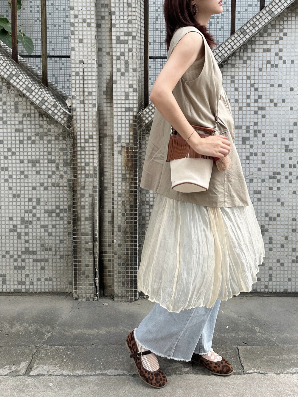 ベージュ系のベスト、ホワイト系のワンピース、ブルー系のデニムパンツを着用したレディースの秋コーディネートの2枚目の写真