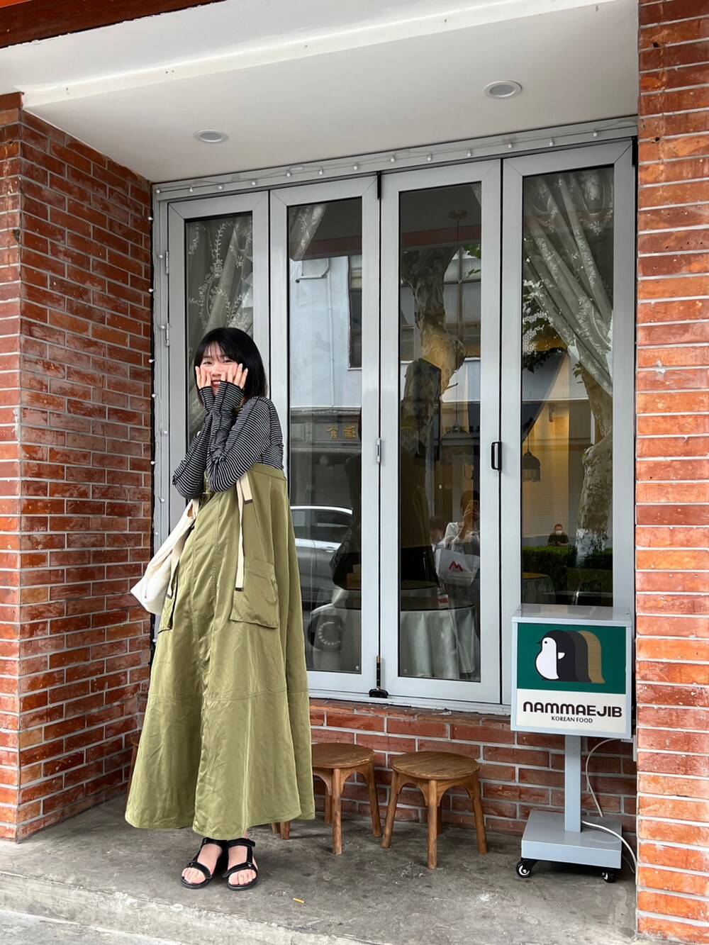 グリーン系のジャンパースカート、ベージュ系のトートバッグ、ブラック系のTシャツ/カットソーを着用したレディースの夏コーディネートの3枚目の写真