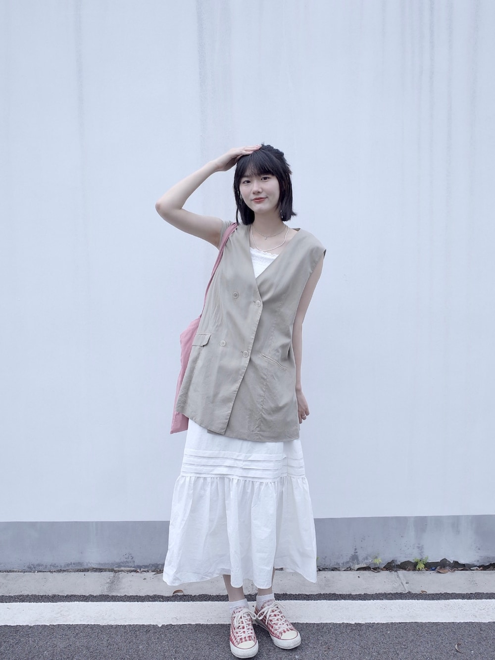 ベージュ系のベスト、ホワイト系のスカート、レッド系のスニーカーを着用したレディースの夏コーディネートの2枚目の写真