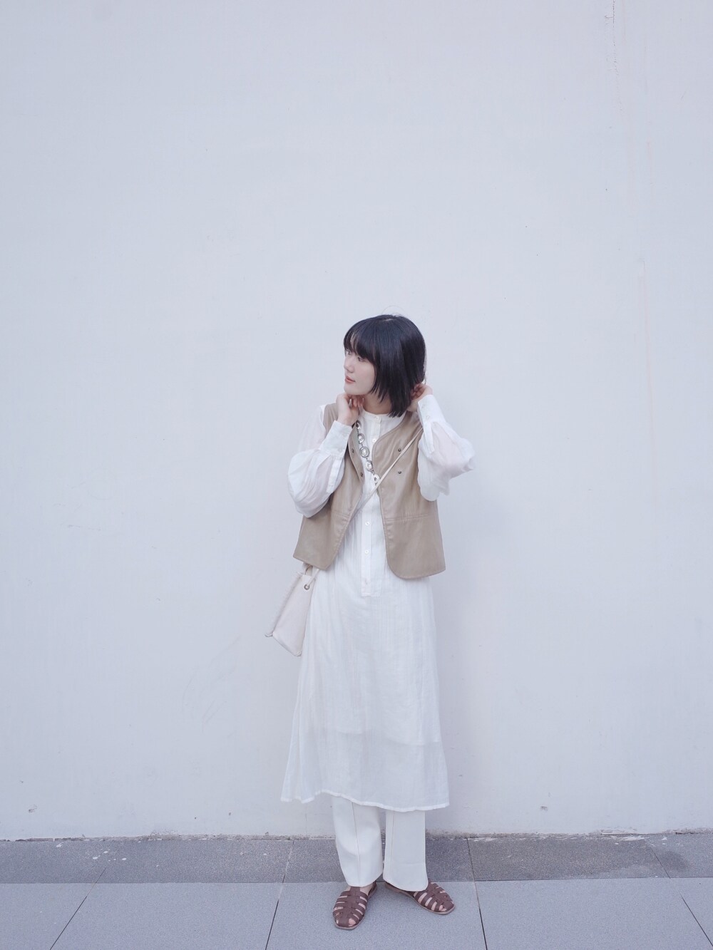 ベージュ系のベスト、ホワイト系のワンピース、ブラウン系のサンダルを着用したレディースの夏コーディネートの3枚目の写真