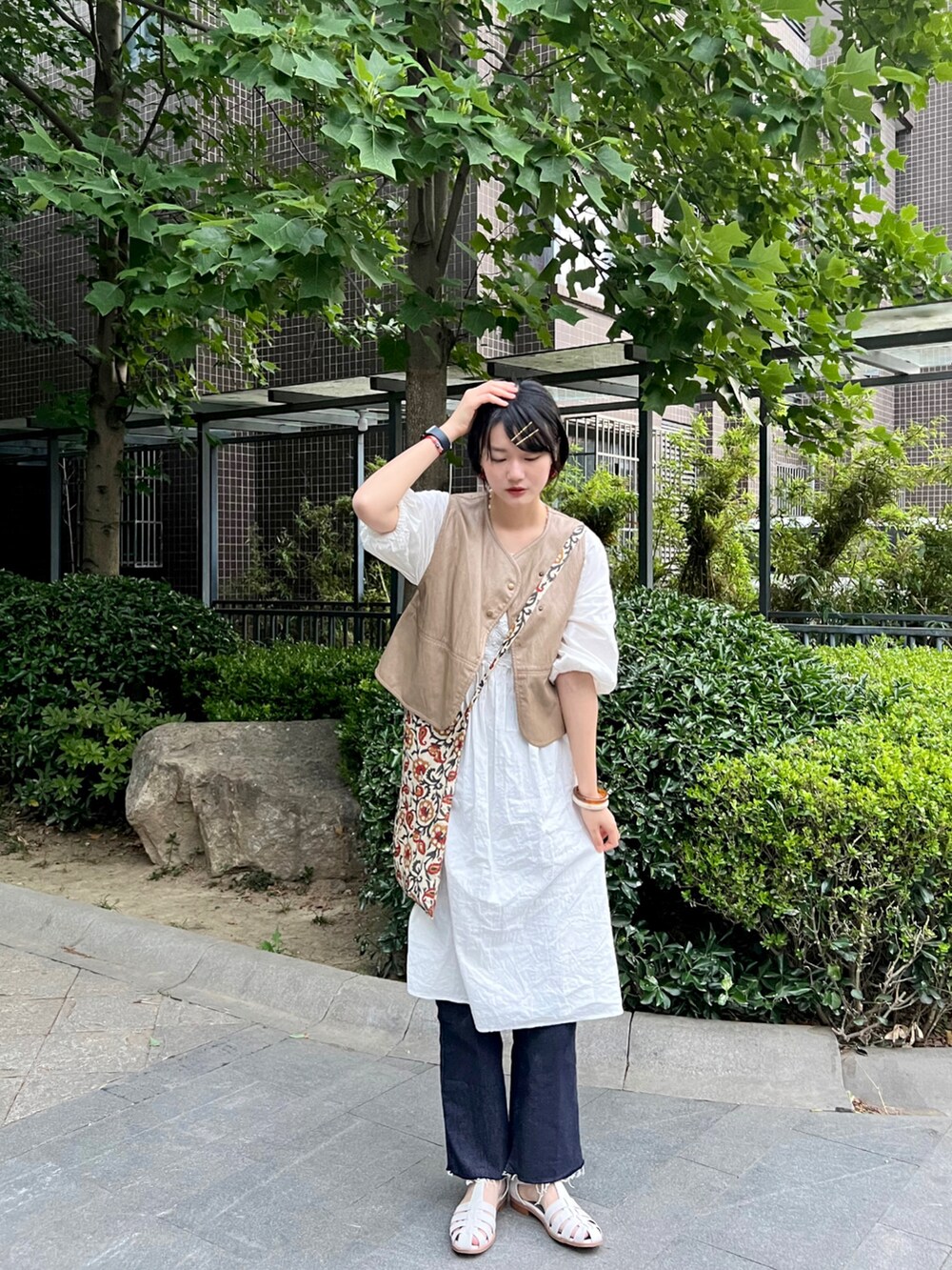 ベージュ系のベスト、ブルー系のデニムパンツ、ホワイト系のサンダルを着用したレディースの春コーディネートの2枚目の写真