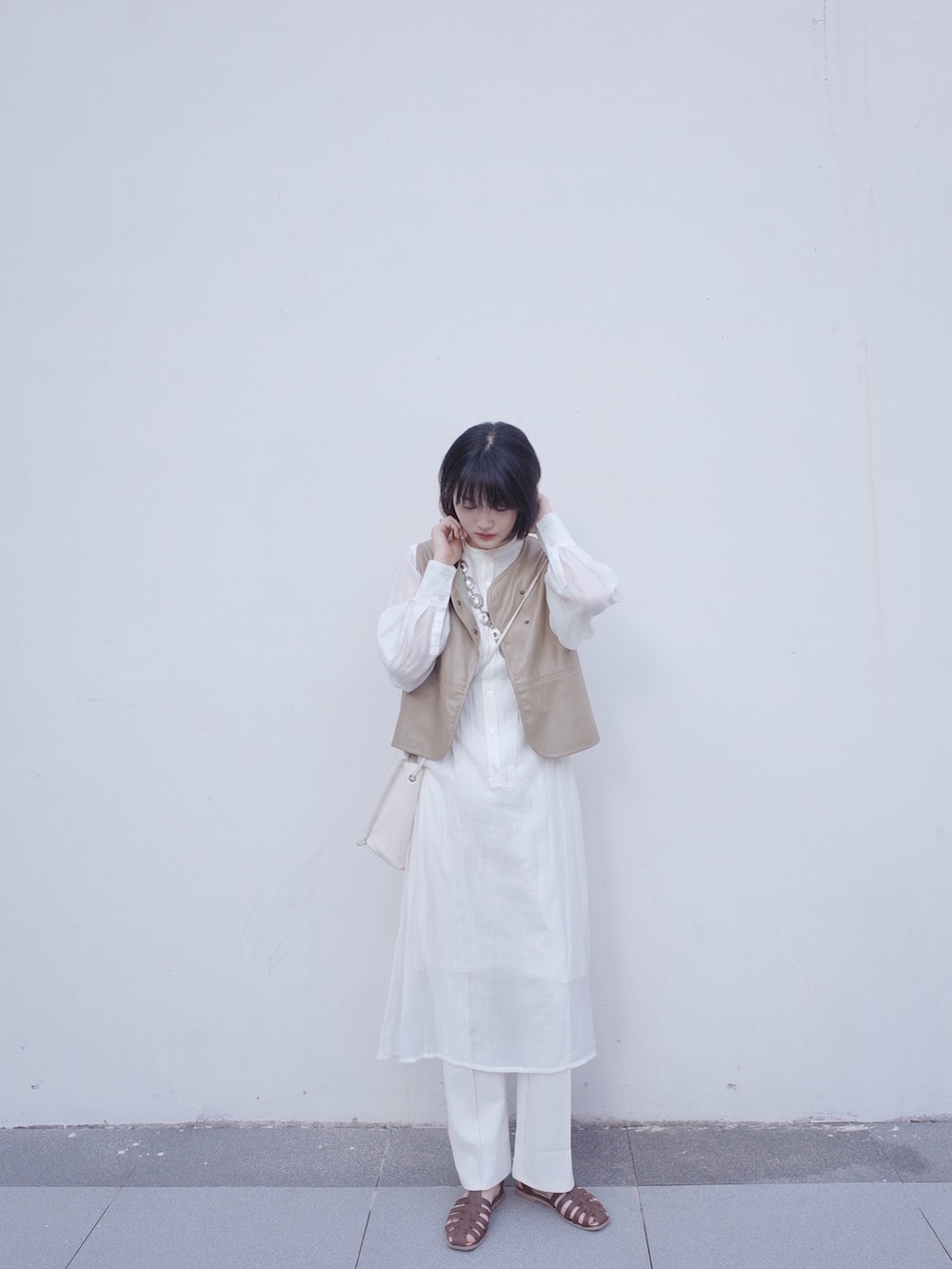 ベージュ系のベスト、ホワイト系のワンピース、ブラウン系のサンダルを着用したレディースの夏コーディネートの2枚目の写真