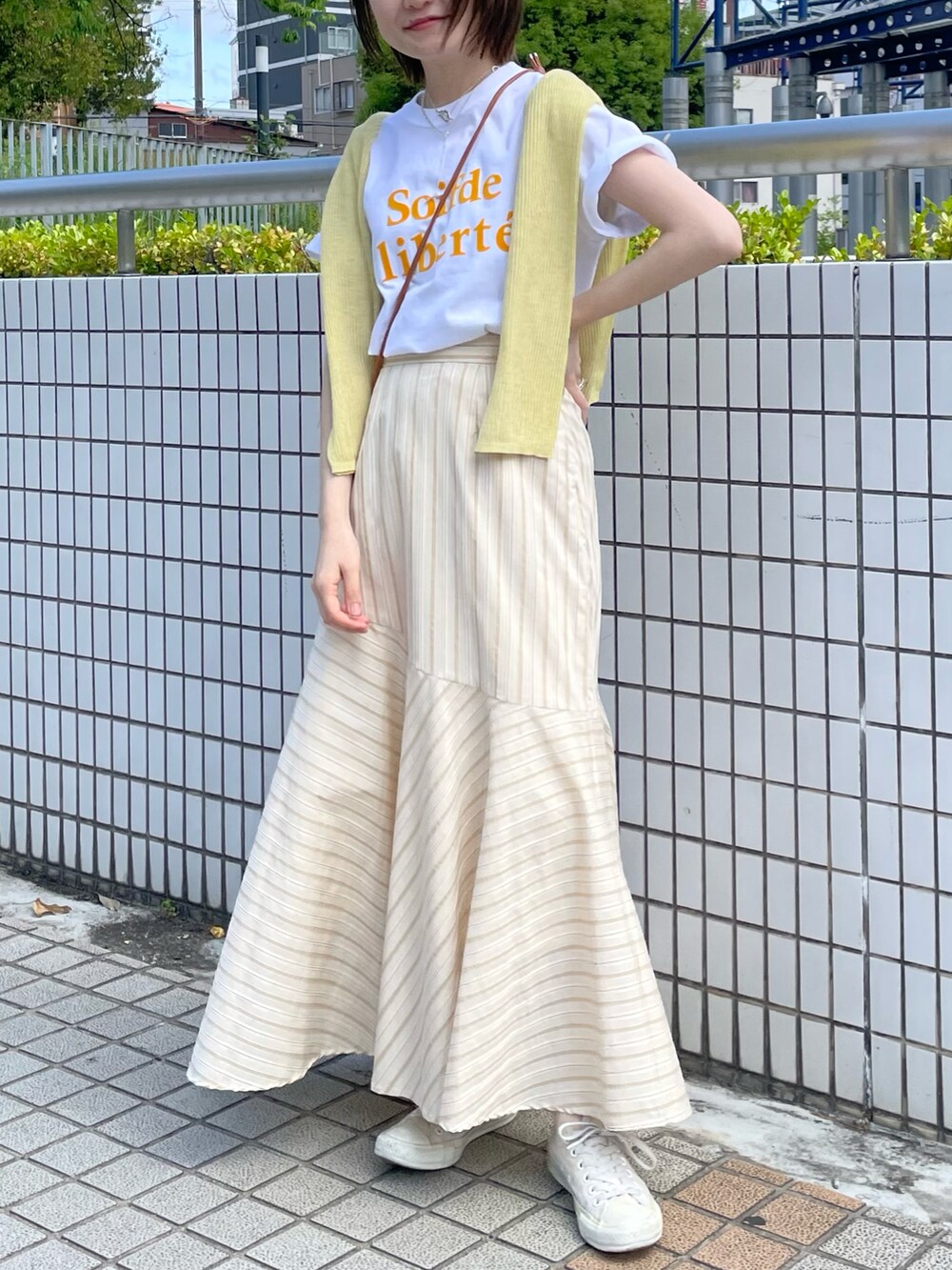 ベージュ系のスカート、オレンジ系のTシャツ/カットソー、イエロー系のニット/セーターを着用したレディースの春コーディネートの4枚目の写真