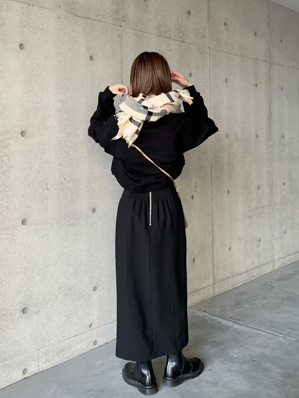 ブラック系のスカート、ブラック系のブーツ、ベージュ系のショルダーバッグを着用したレディースの冬コーディネートの3枚目の写真