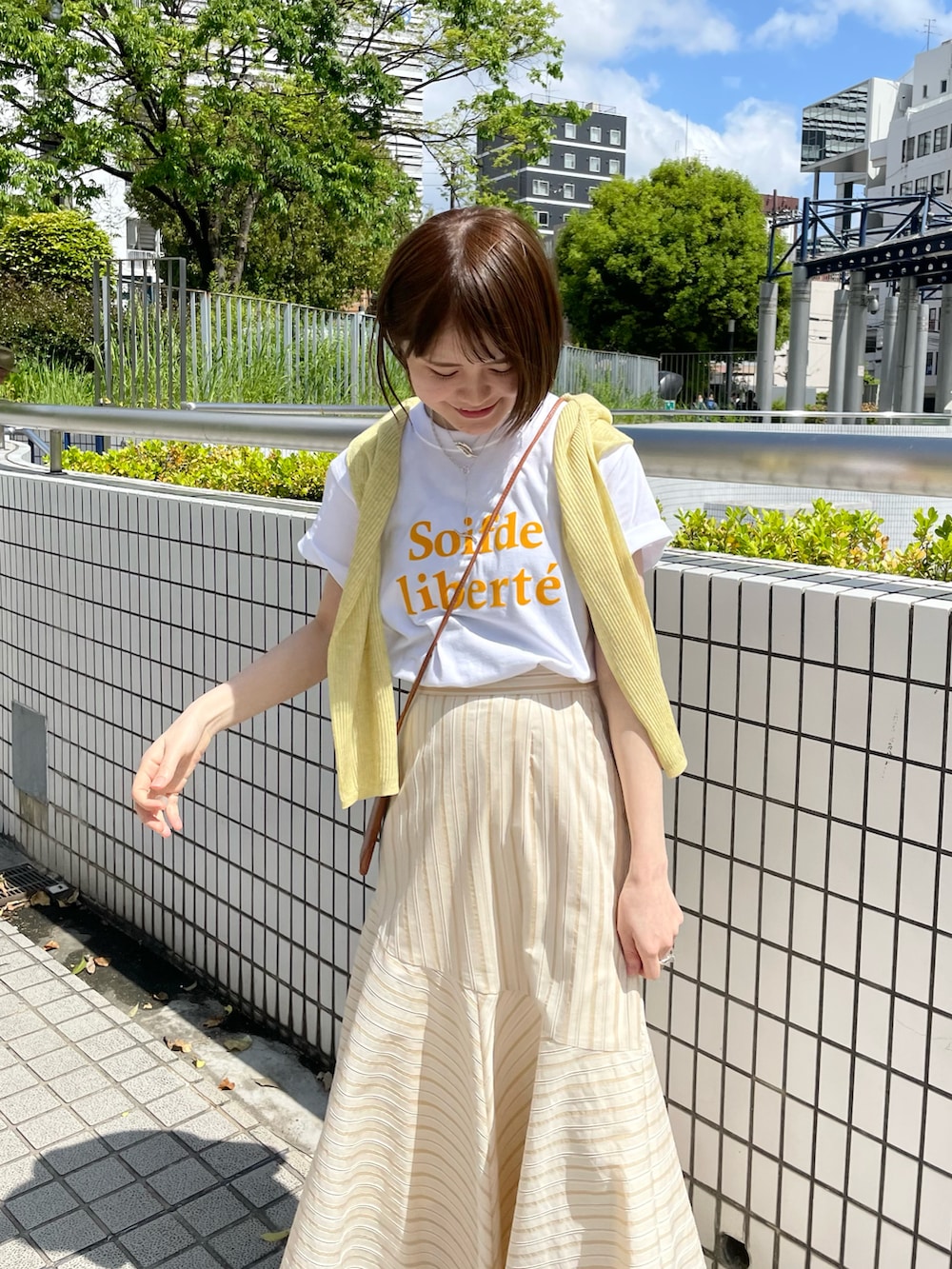 ベージュ系のスカート、オレンジ系のTシャツ/カットソー、イエロー系のニット/セーターを着用したレディースの春コーディネートの3枚目の写真