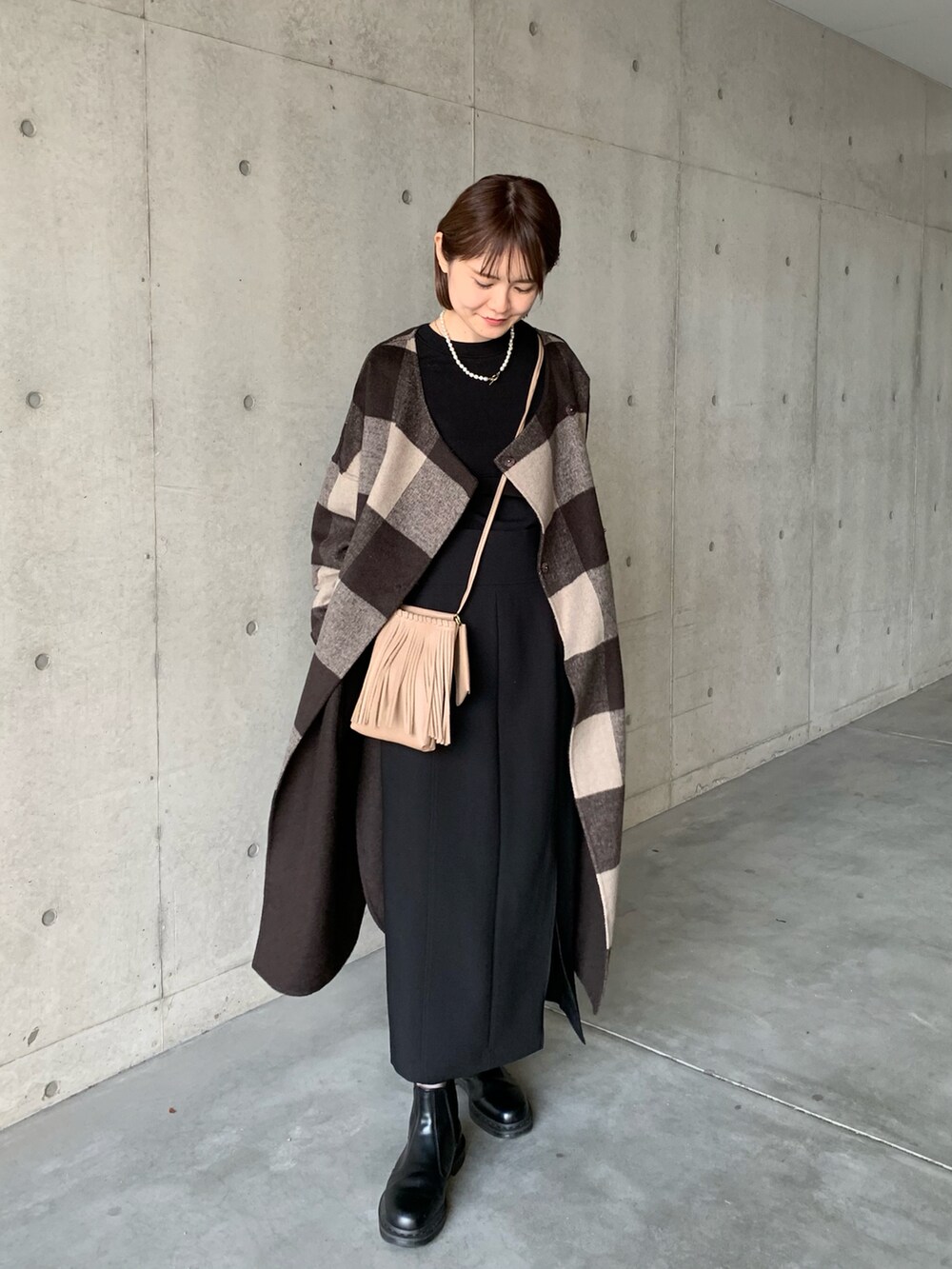 ブラック系のブーツ、ブラウン系のノーカラーコート、ブラック系のスカートを着用したレディースの秋コーディネートの2枚目の写真