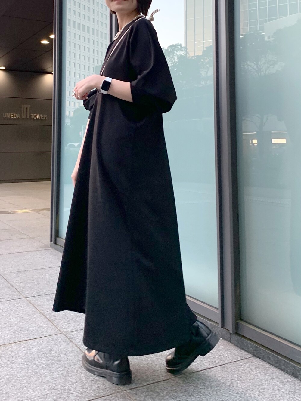 ブラック系のワンピース、ホワイト系のショルダーバッグ、ブラック系のブーツを着用したレディースの冬コーディネートの2枚目の写真