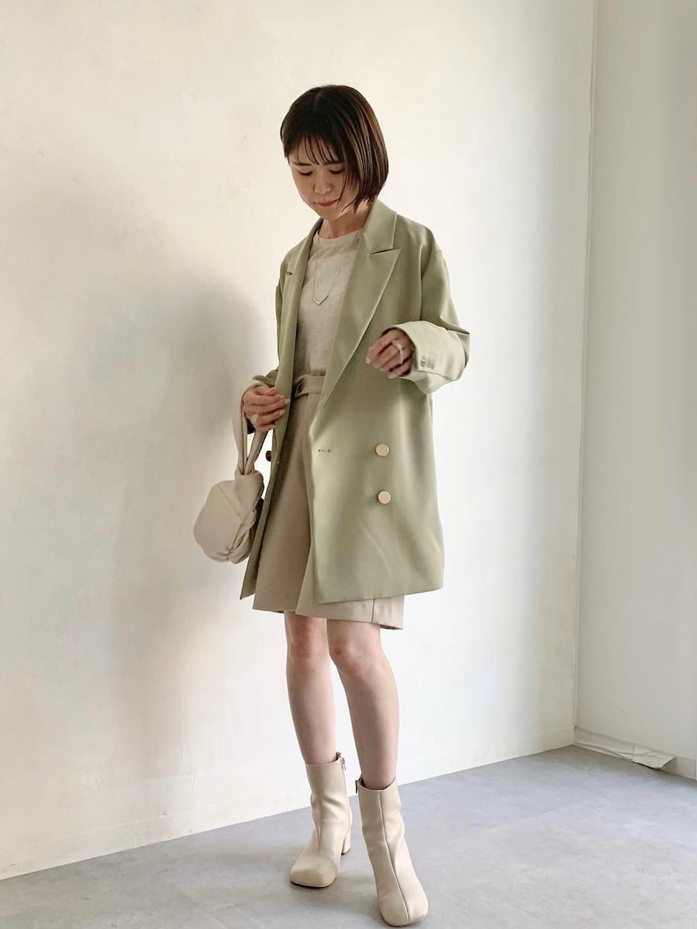 グリーン系のテーラードジャケット、ベージュ系のニット/セーター、ホワイト系のハンドバッグを着用したレディースの春コーディネートの4枚目の写真