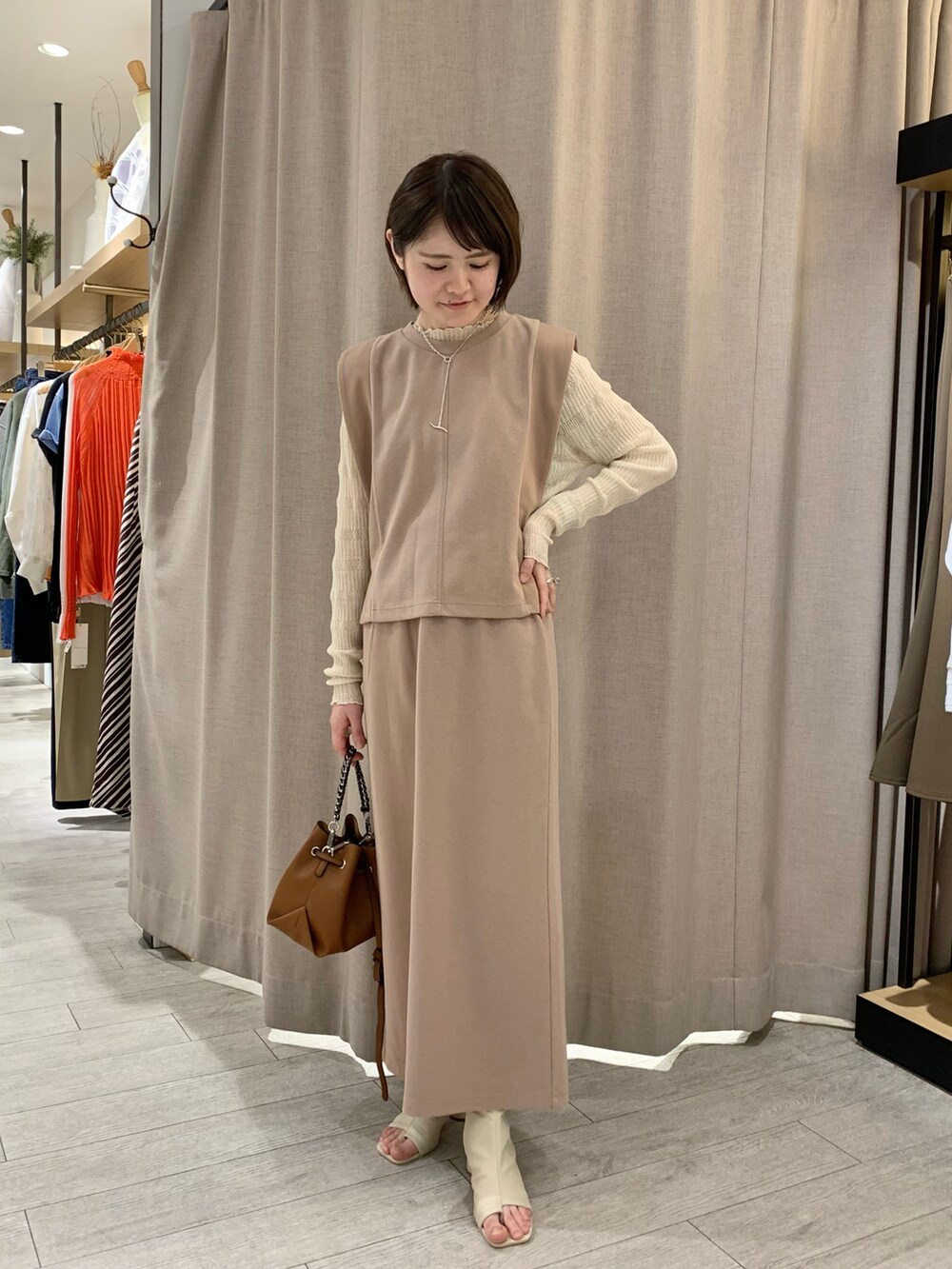 ベージュ系のベスト、ベージュ系のスカート、ホワイト系のニット/セーターを着用したレディースの春コーディネートの3枚目の写真