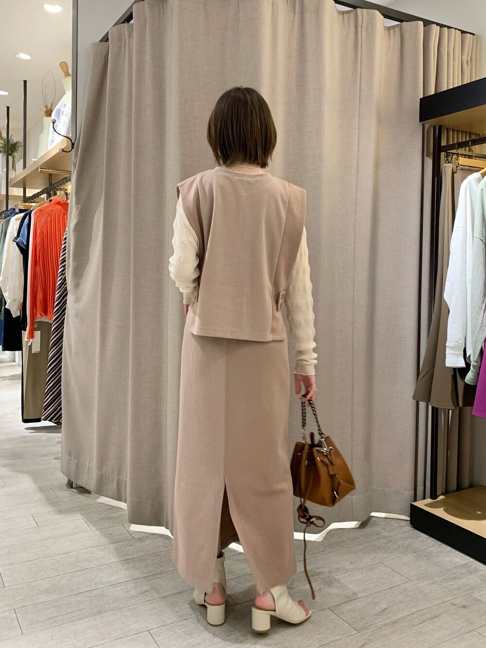 ベージュ系のベスト、ベージュ系のスカート、ホワイト系のニット/セーターを着用したレディースの春コーディネートの2枚目の写真