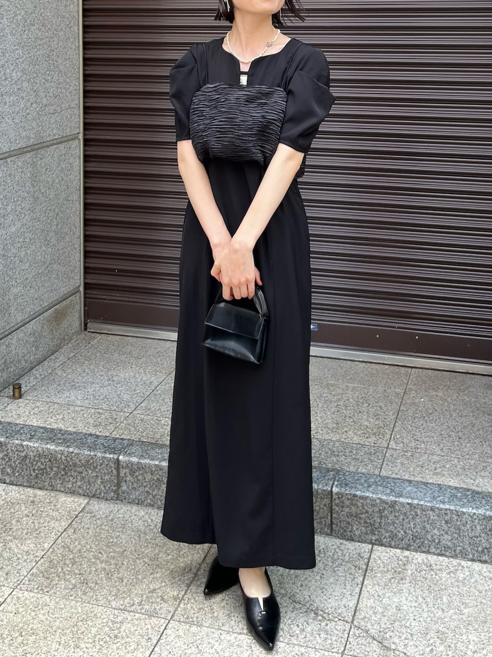 ブラック系のワンピース、ブラック系のパンプス、ブラック系のバッグを着用したレディースの夏コーディネートの2枚目の写真