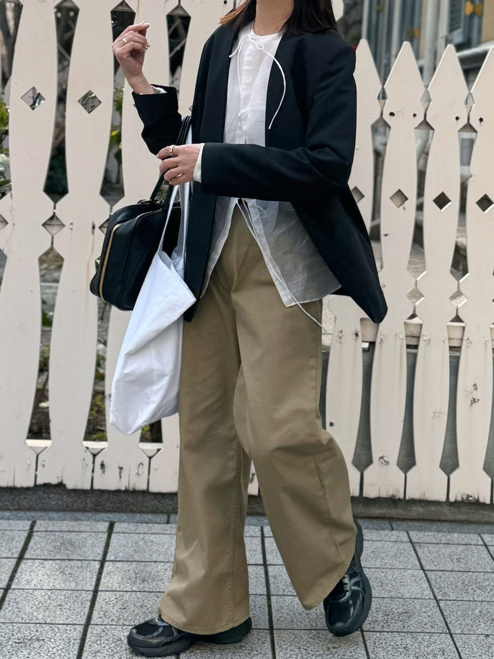 ブラック系のバッグ、ブラック系のノーカラージャケット、ベージュ系のチノパンツを着用したレディースの春コーディネートの2枚目の写真
