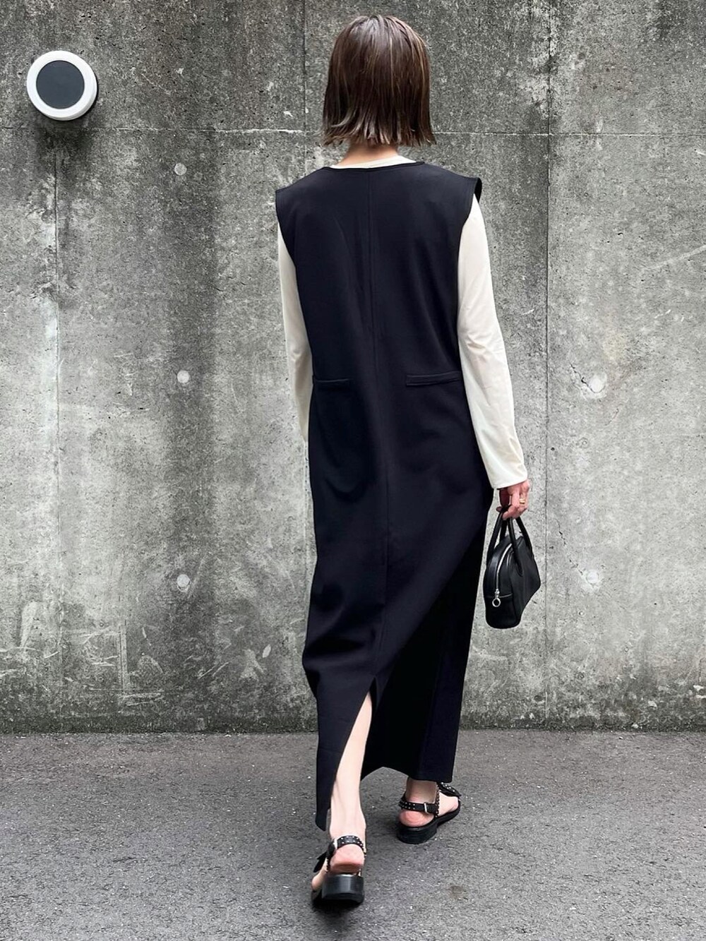 ブラック系のジャンパースカート、ブラック系のボストンバッグ、ブラック系のサンダルを着用したレディースの春コーディネートの3枚目の写真