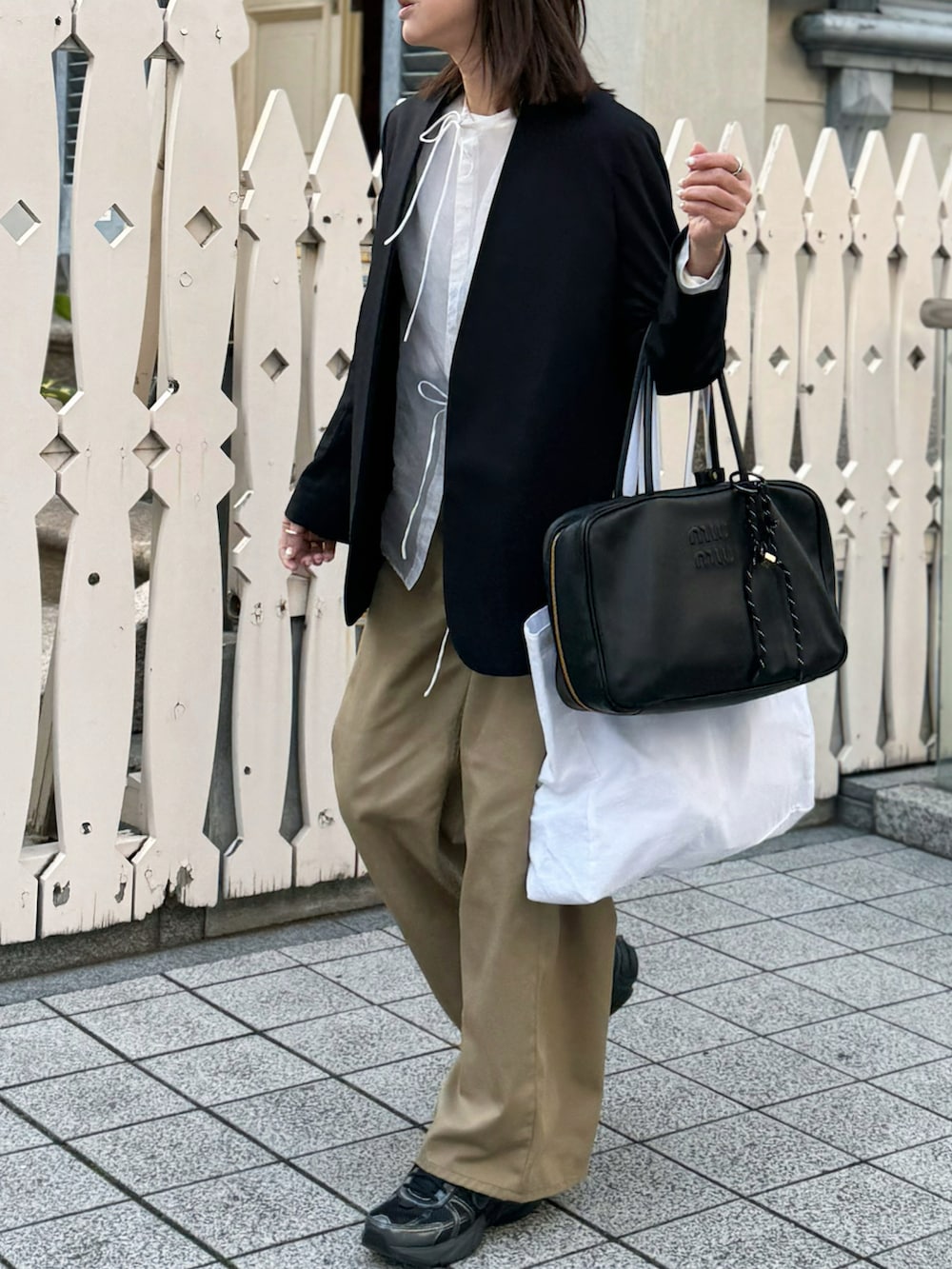 ブラック系のバッグ、ブラック系のノーカラージャケット、ベージュ系のチノパンツを着用したレディースの春コーディネートの4枚目の写真