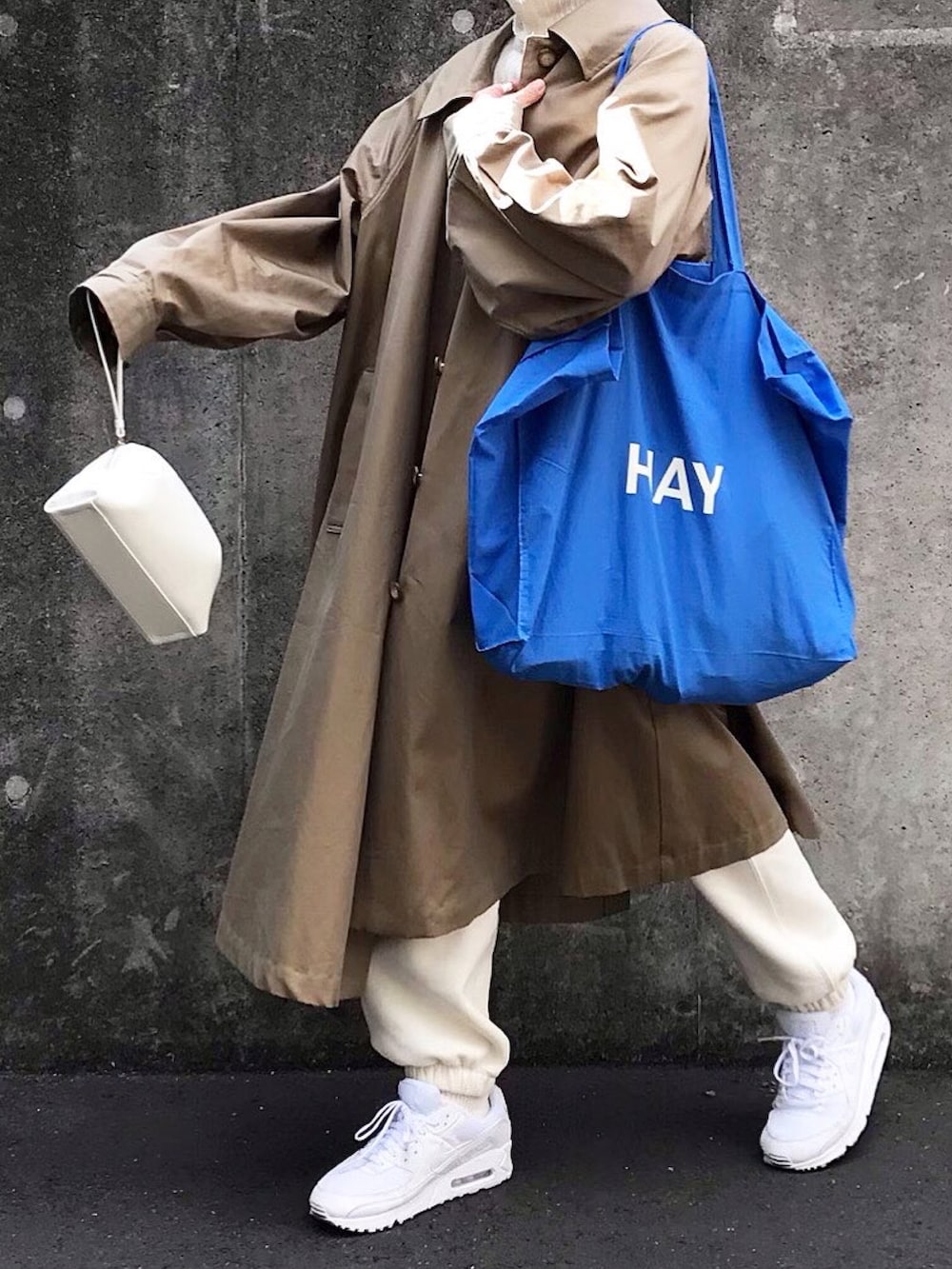 ホワイト系のショルダーバッグ、ベージュ系のステンカラーコート、ホワイト系のスニーカーを着用したレディースの春コーディネートの2枚目の写真