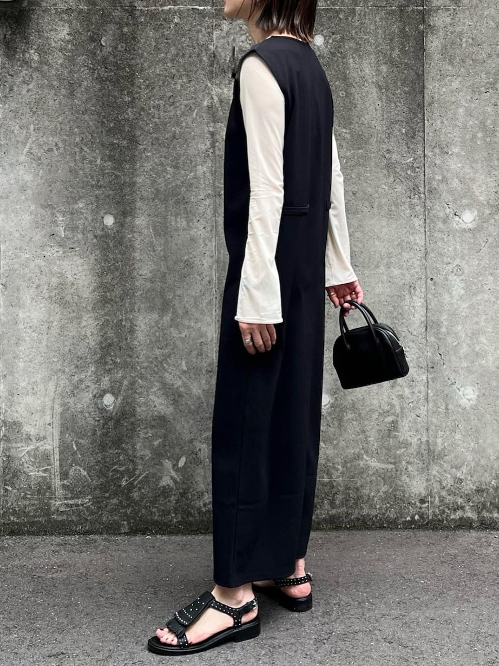 ブラック系のジャンパースカート、ブラック系のボストンバッグ、ブラック系のサンダルを着用したレディースの春コーディネートの2枚目の写真