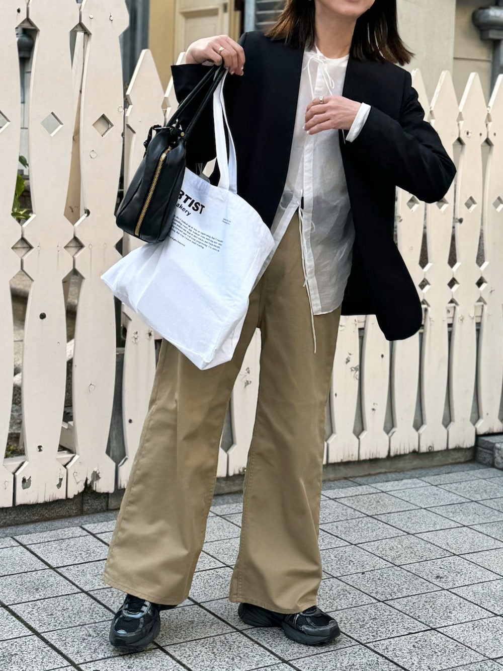 ブラック系のバッグ、ブラック系のノーカラージャケット、ベージュ系のチノパンツを着用したレディースの春コーディネートの3枚目の写真