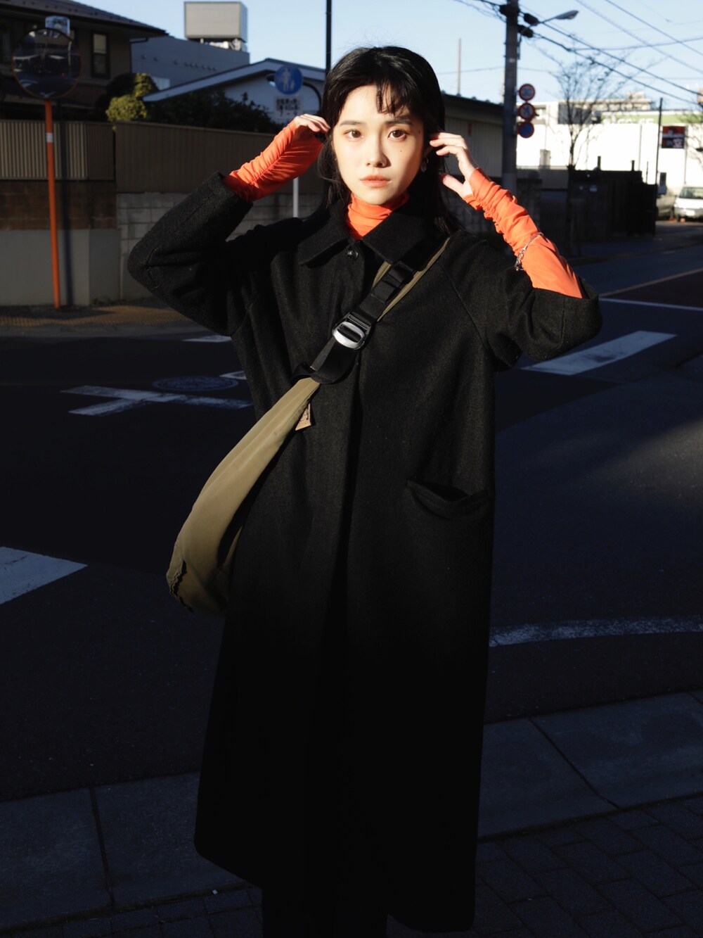 オレンジ系のTシャツ/カットソー、ブラック系のステンカラーコートを着用したレディースの冬コーディネートの2枚目の写真