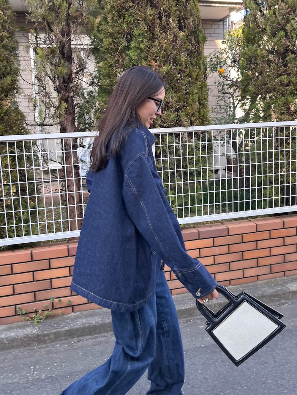 ブルー系のカバーオール、ブルー系のデニムパンツ、ホワイト系のハンドバッグを着用したレディースの春コーディネートの2枚目の写真