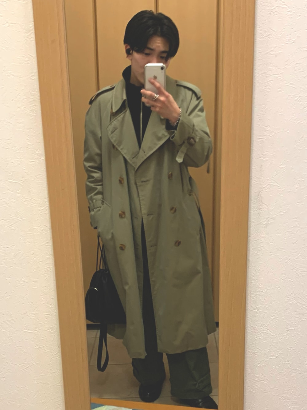 ベージュ系のトレンチコート、ブラック系のニット/セーター、ブラック系のショルダーバッグを着用したメンズの冬コーディネートの2枚目の写真