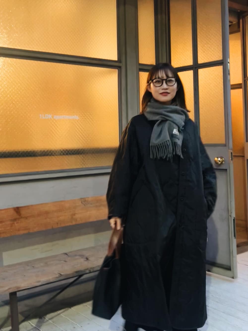 ブラック系のハンドバッグ、ブラック系のスニーカー、グレー系のマフラーを着用したレディースの春コーディネートの2枚目の写真