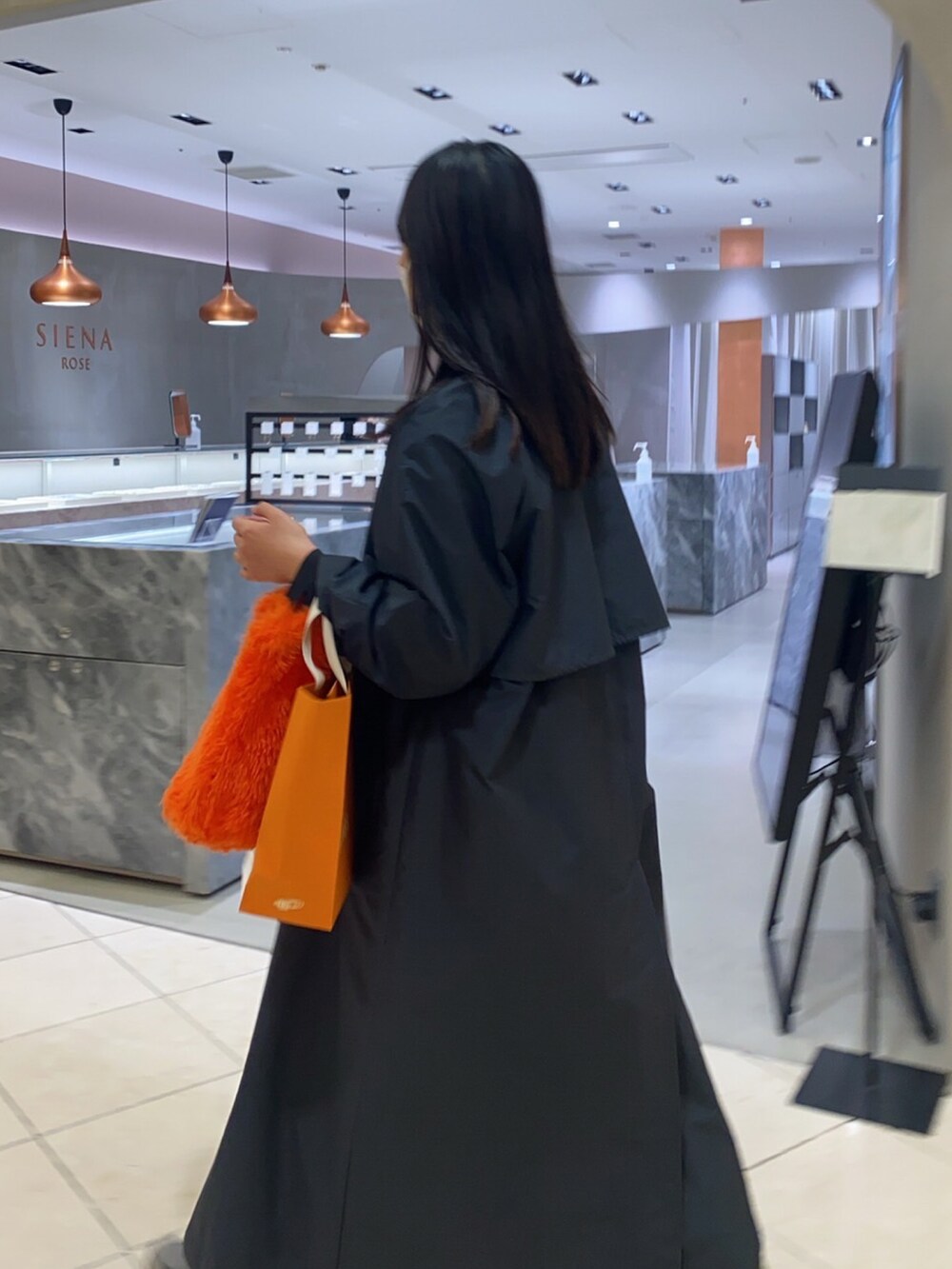 オレンジ系のハンドバッグ、イエロー系のカーディガン/ボレロ、ブラック系のステンカラーコートを着用したレディースの冬コーディネートの2枚目の写真