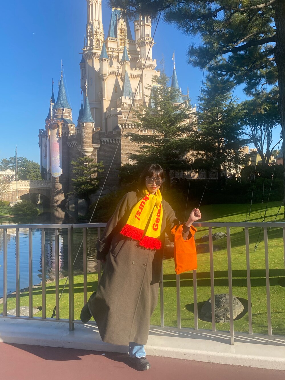 オレンジ系のトートバッグ、ブラウン系のジャケット/アウター、ブラック系のスニーカーを着用したレディースの冬コーディネートの2枚目の写真