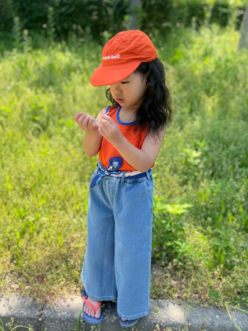 オレンジ系のタンクトップ、ブルー系のデニムパンツ、ブルー系のサンダルを着用したキッズの夏コーディネートの2枚目の写真