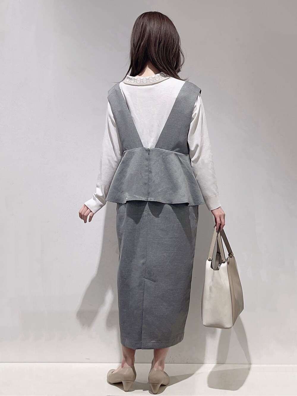 グレー系のワンピース、ホワイト系のニット/セーター、ベージュ系のトートバッグを着用したレディースの春コーディネートの3枚目の写真