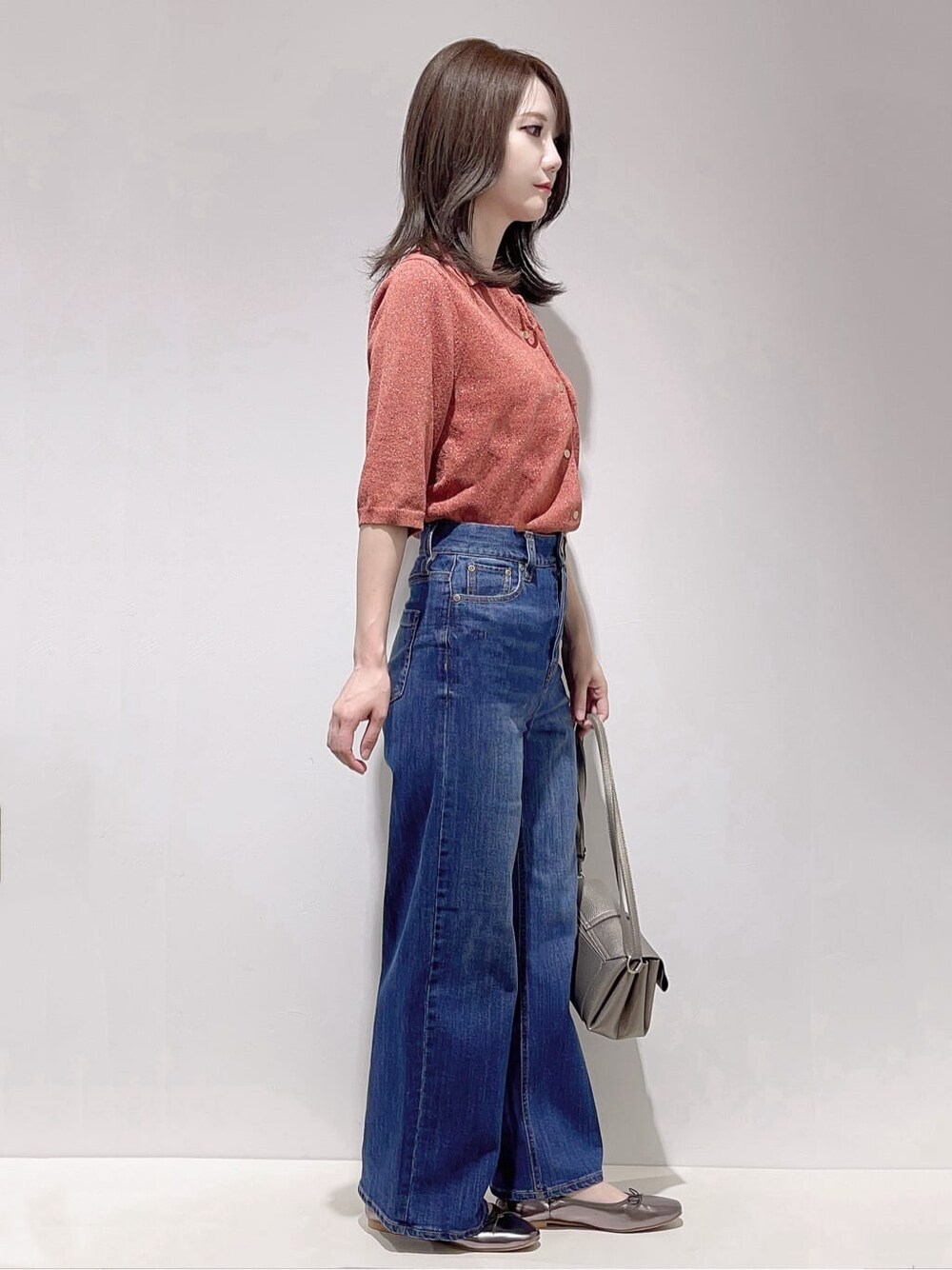 レッド系のニット/セーター、ブルー系のデニムパンツ、シルバー系のショルダーバッグを着用したレディースの秋コーディネートの2枚目の写真
