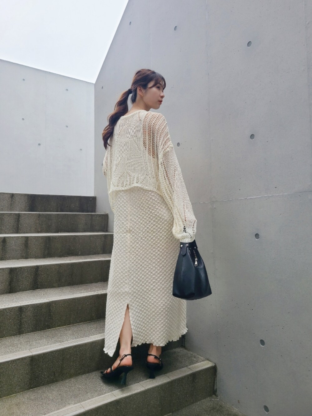 ブラック系のサンダル、ホワイト系のワンピース、ゴールド系のピアス（両耳用）を着用したレディースの春コーディネートの3枚目の写真