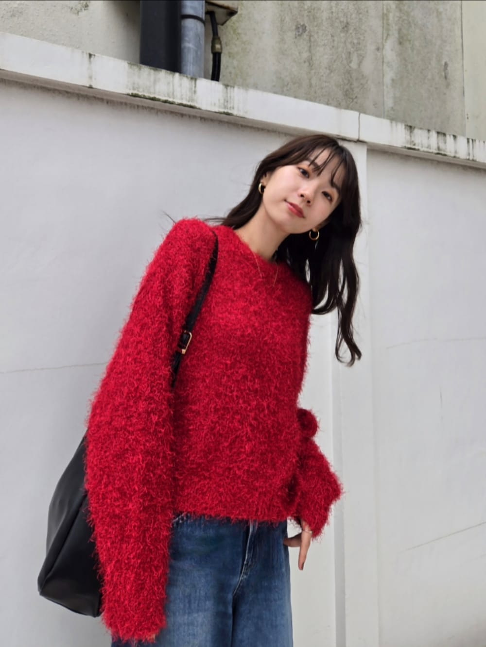 レッド系のニット/セーター、ブラック系のトートバッグ、ブルー系のデニムパンツを着用したレディースの秋コーディネートの2枚目の写真