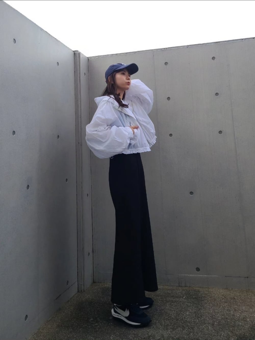 ブラック系のハンドバッグ、ホワイト系のナイロンジャケット、ブルー系のスニーカーを着用したレディースの春コーディネートの2枚目の写真