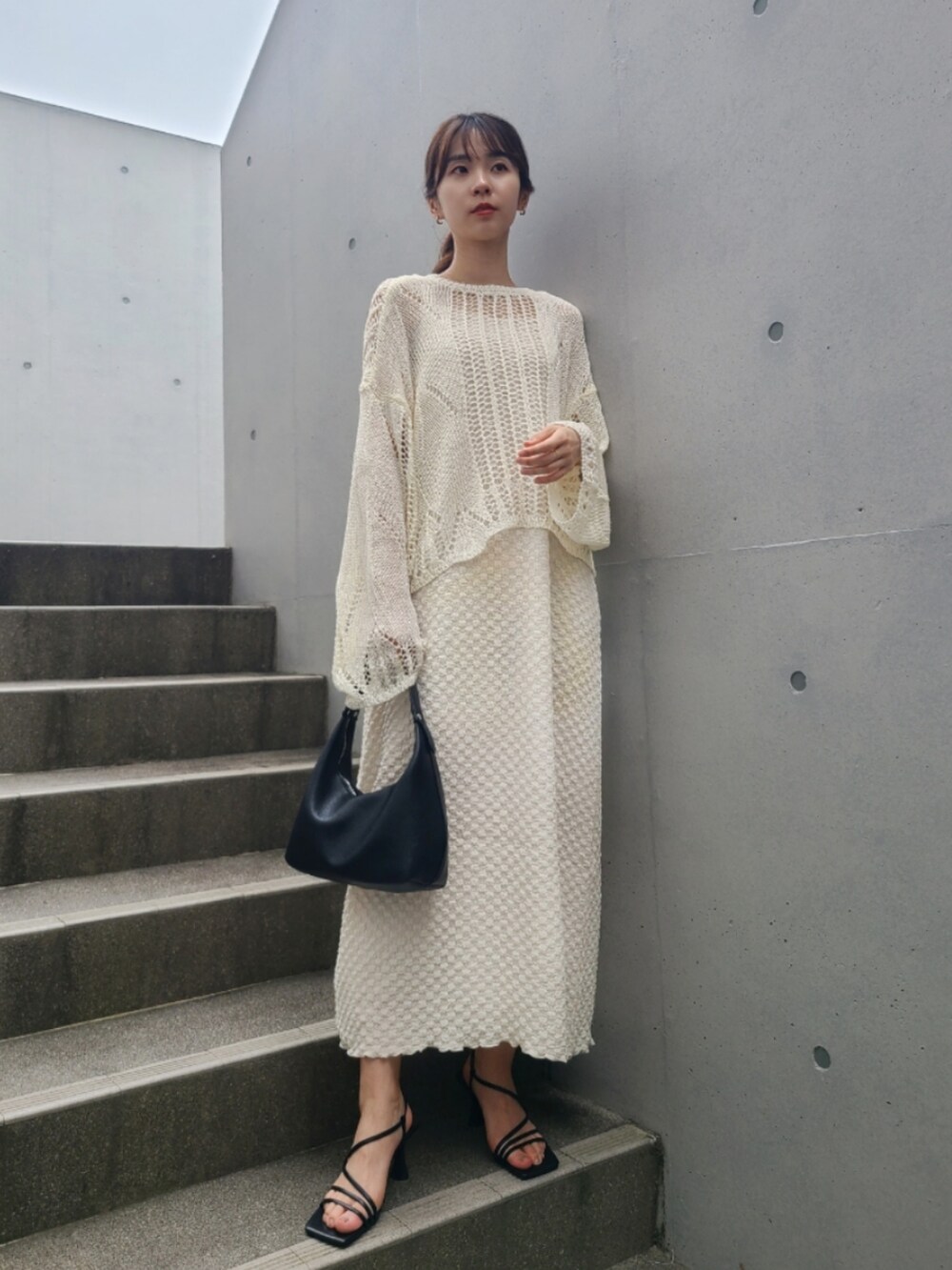 ブラック系のサンダル、ホワイト系のワンピース、ゴールド系のピアス（両耳用）を着用したレディースの春コーディネートの2枚目の写真