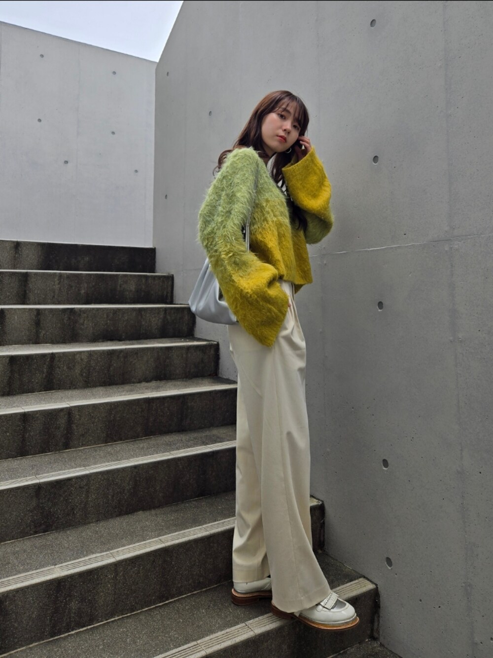 イエロー系のニット/セーター、シルバー系のハンドバッグ、ホワイト系のパンツを着用したレディースの秋コーディネートの3枚目の写真